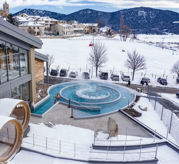 ensemble de personnes profitant de la piscine extérieur en hiver avec une montagne eneigé et un village derriere