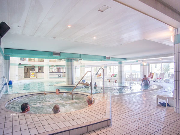 ensemble de personnes profitant de la piscine extérieur en hiver avec une montagne eneigé et un village derriere