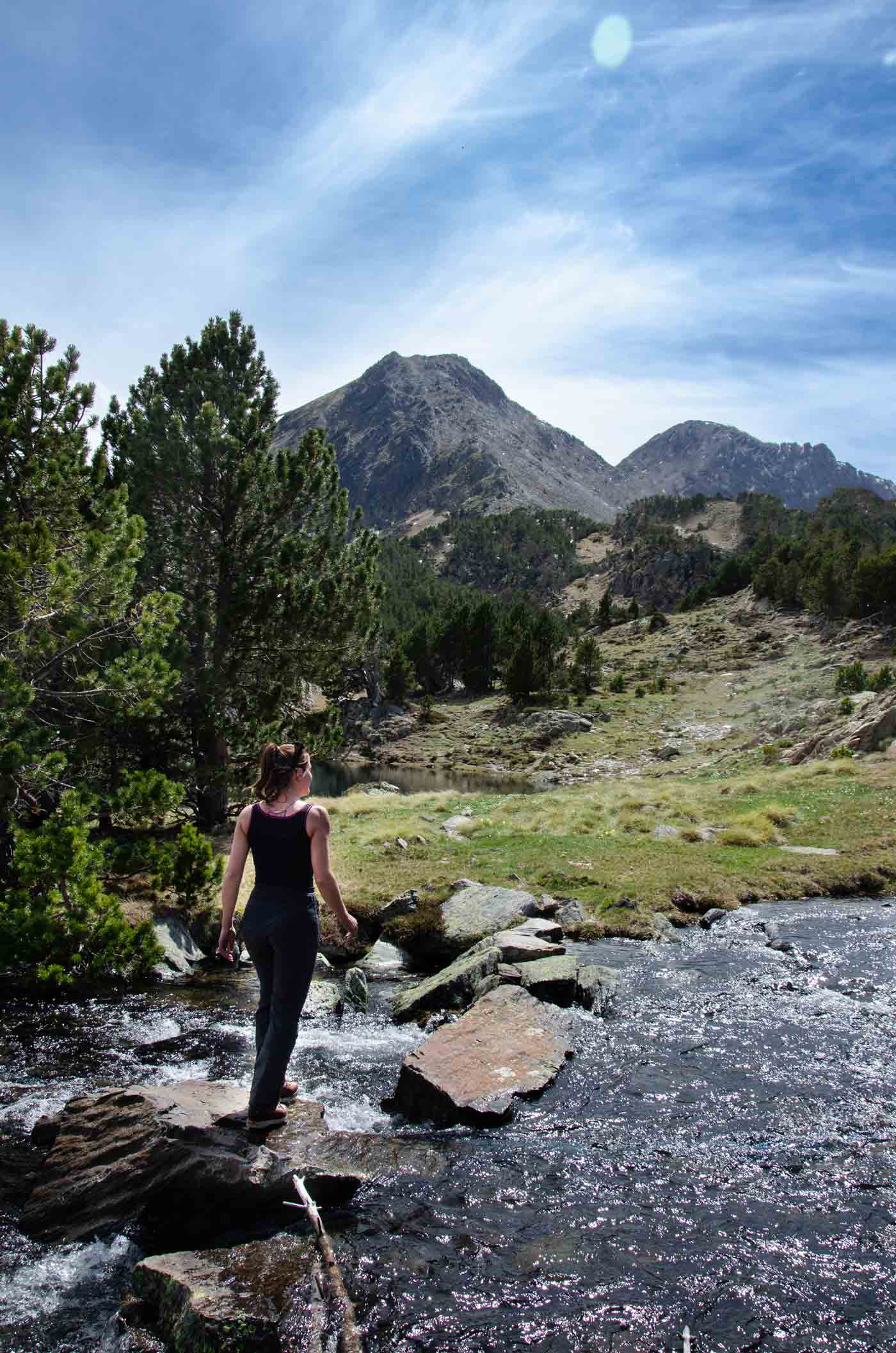Randonnée au Camporells Femme traversant une rivière. Elle regarde une montagne au loin, le Pic Pérics